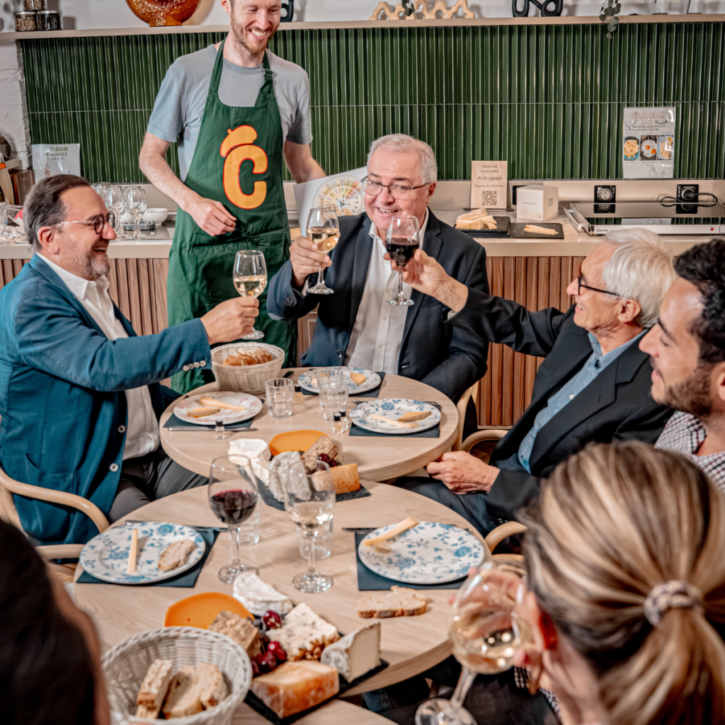 Groupe de collègues souriants autour d'une table de dégustation, verres à la main, dans une cave ou salle de réception toulousaine.